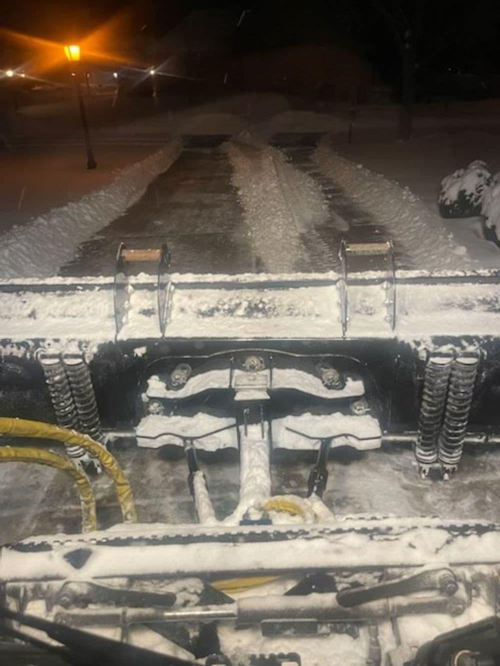 View from a snow plow clearing a snowy residential driveway at night.